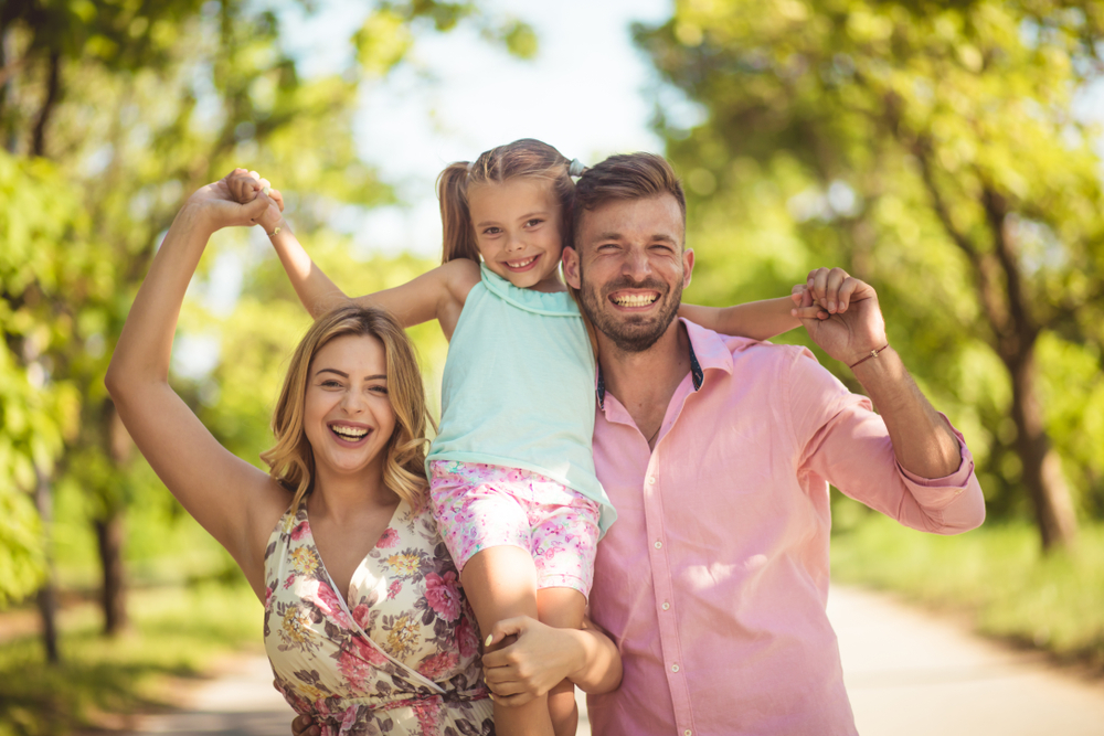 Smiling parents carrying their child outdoors while showing bright, healthy smiles, representing family-friendly dental care in National City CA - Dentist National City CA