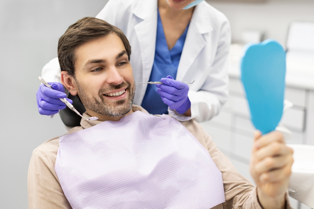 Male patient holding a mirror and smiling during a dental appointment while dentist works, highlighting successful treatment at a dentist in National City CA - Dentist National City CA